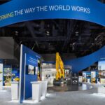 Trade show exhibit featuring a dynamic branded environment with a blue structure showcasing construction technology and information displays